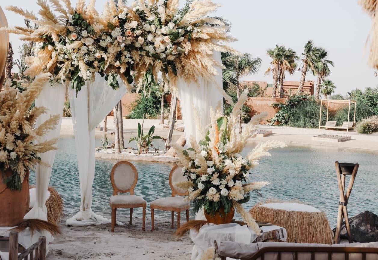 Arche de mariage en pampa et roses blanches au bord d’un lagon de sable