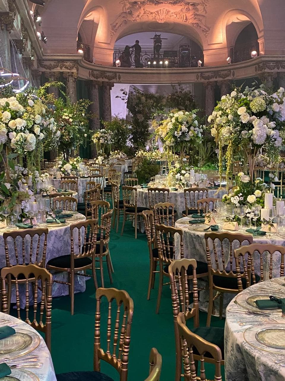 Salle de réception de type palais aux colonnes et tapis émeraude, tables rondes élégamment dressées