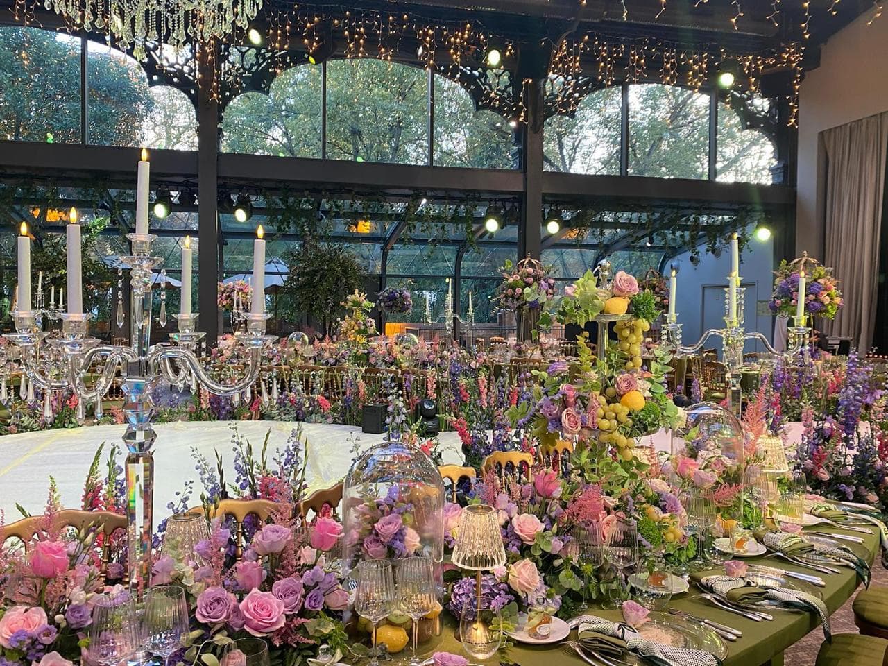 Table de mariage foisonnante de fleurs roses, violettes et vertes sous une verrière